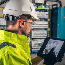 Man, an electrical technician working in a switchboard with fuses. Installation and connection of electrical equipment. Professional uses a tablet.